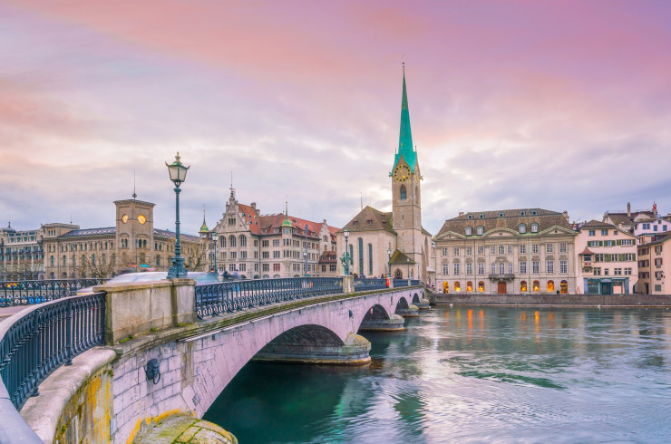 White and beige Swiss buildings along a river, with an archway bridge