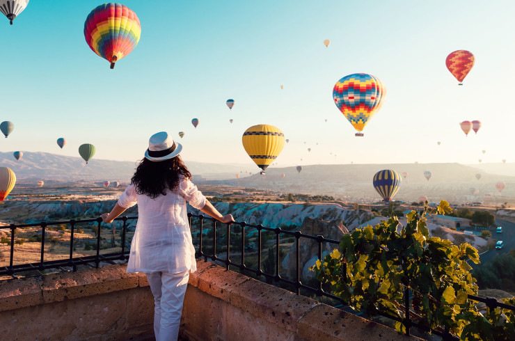 Person in white standing on a balcony looking at hot air balloons 