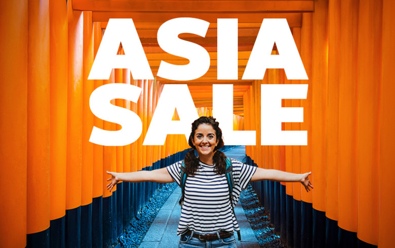 A smiling traveler stands with arms outstretched along a pathway of vibrant orange torii gates at a Japanese shrine, wearing a striped shirt and backpack. Bold white text at the top reads “ASIA SALE.”
