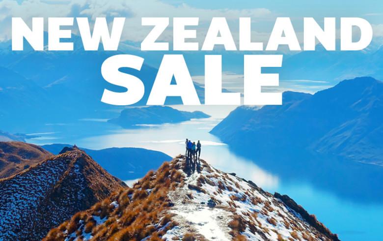 Group of 4 people at the top of a grassy mountain tipped with snow, overlooking mountains and rivers in New Zealand