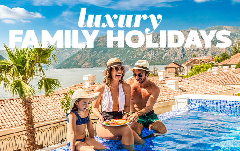 Family of three sitting in an infinity pool laughing and eating fruit in a coastal Greek town featuring luxury family holidays
