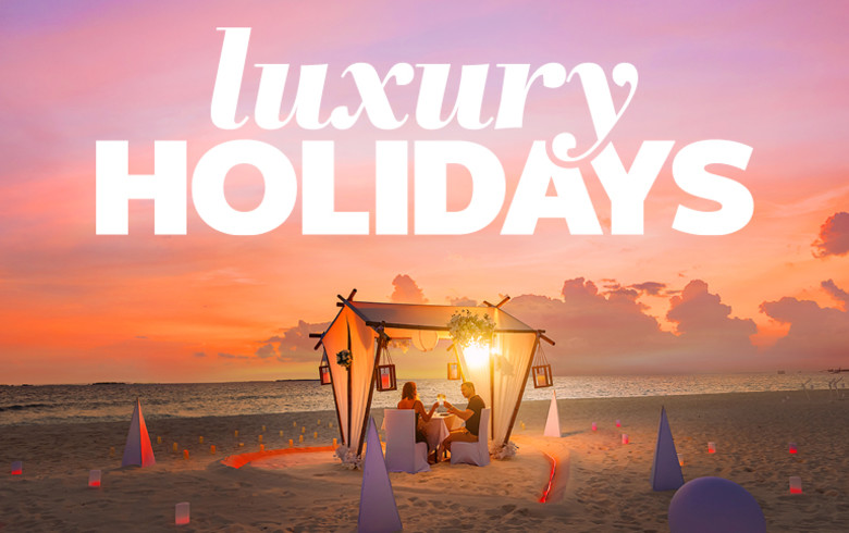Couple having a candle-lit dinner on a beach at sunset featuring luxury holidays
