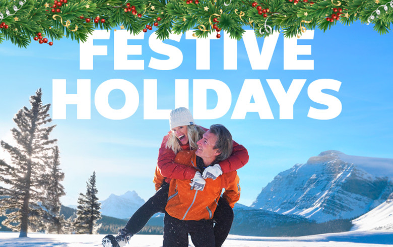 Couple playing in the snow framd by mountains and pine trees featuring festive holidays
