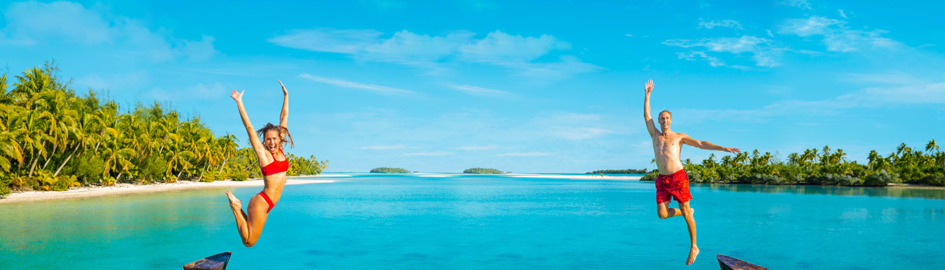 Two people in red swimsuits jumping for joy with tropical beach islands in the background