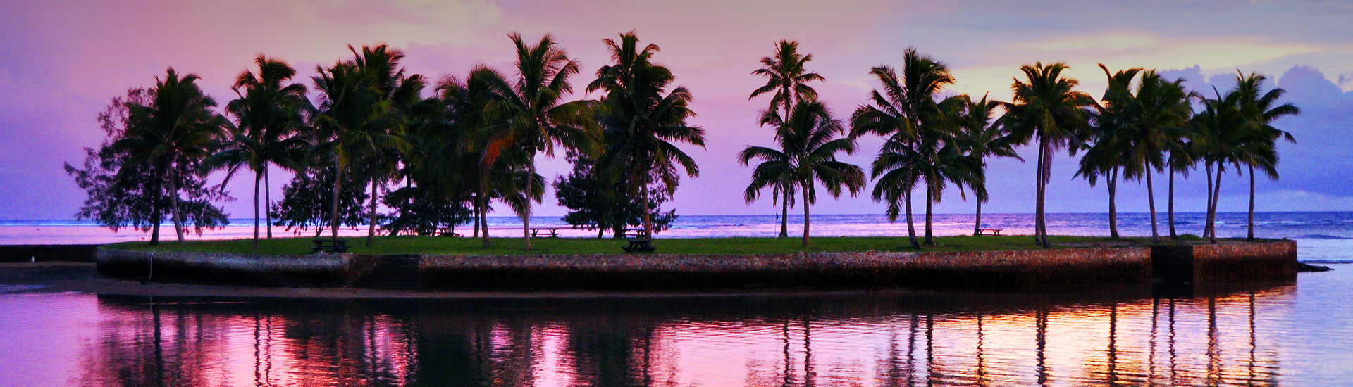 Small tropical island covered in palm trees during a purple sunset