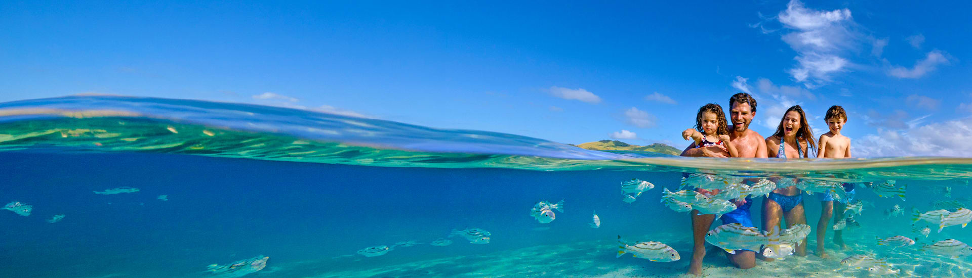 Family of four playing in shallow, clear ocean water