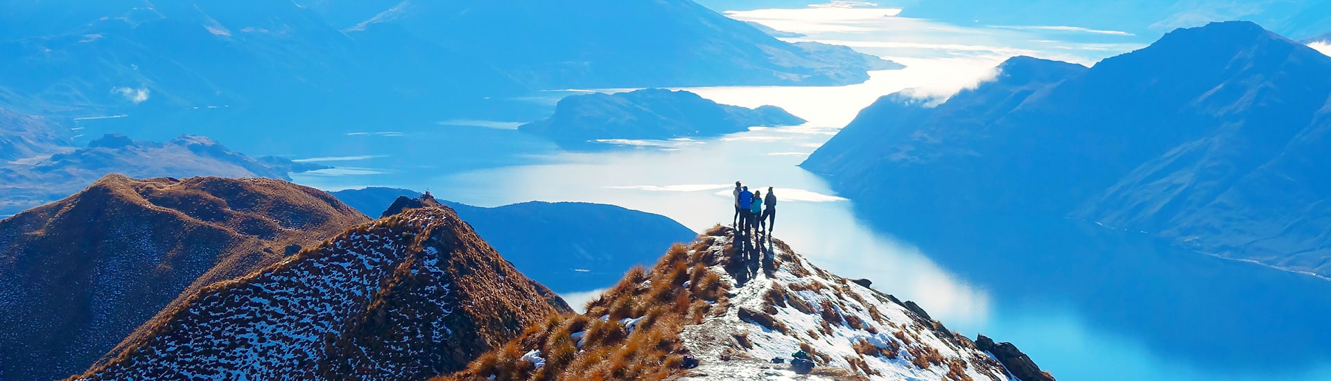 Hikers at the top of a snow-capped mountain looking out at the landscape of New Zealand