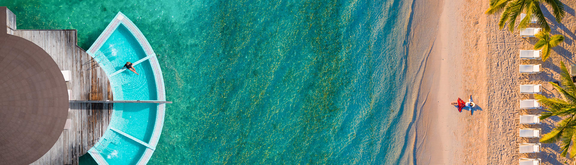 Aerial view of a swimmer in an overwater bungalow pool beside a palm lined beach for member only hotel deals book online and save