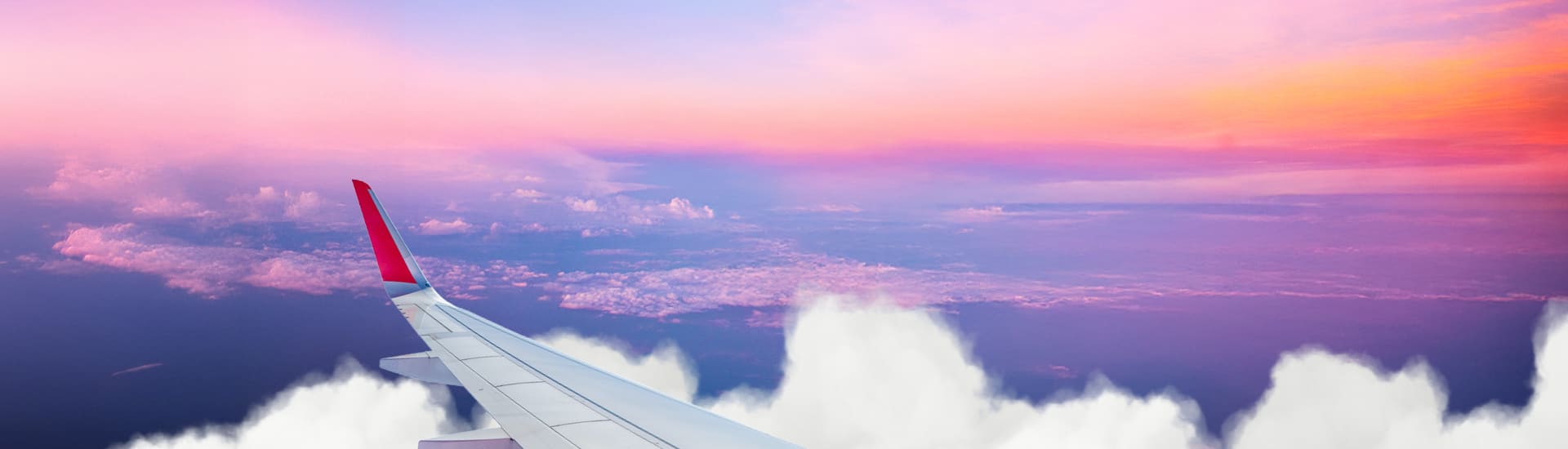 Aeroplane wing soaring above clouds beneath a vivid pink and orange sunset sky