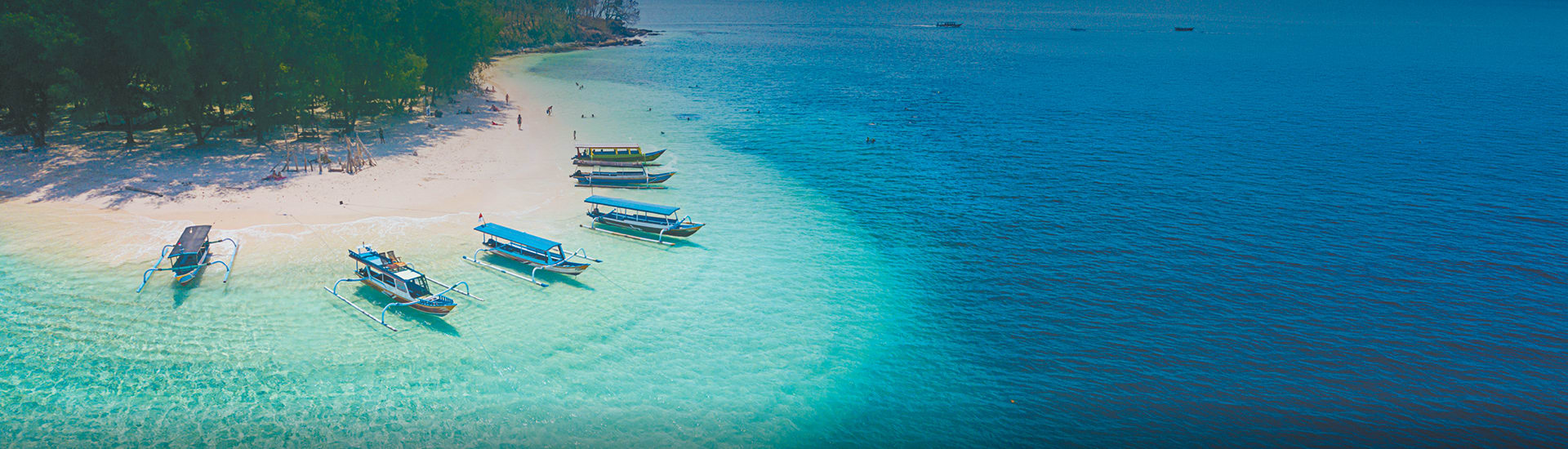 Aerial view of traditional outrigger boats resting in turquoise shallows along a palm fringed tropical beach