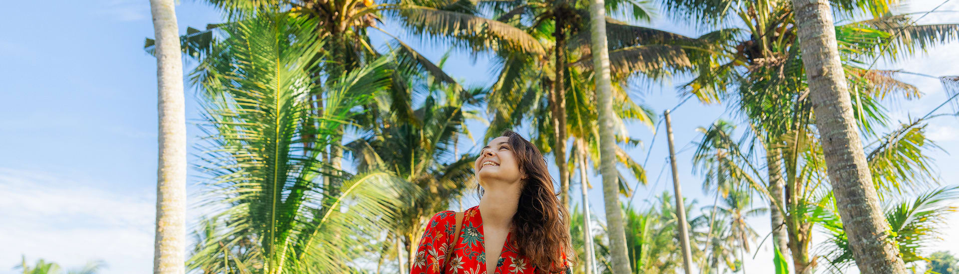 A happy woman in a red top under palm trees
