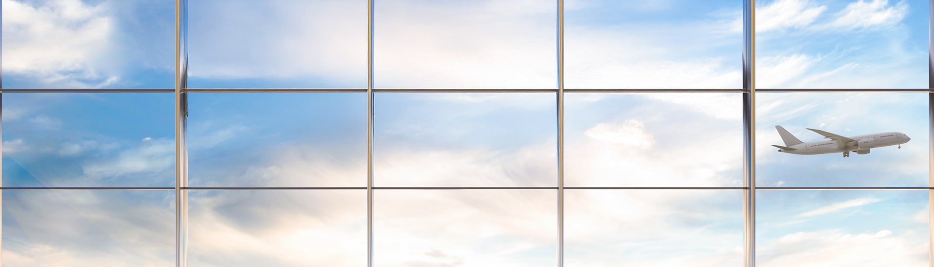 Large window looking out at a plane flying through a cloud-filled sky