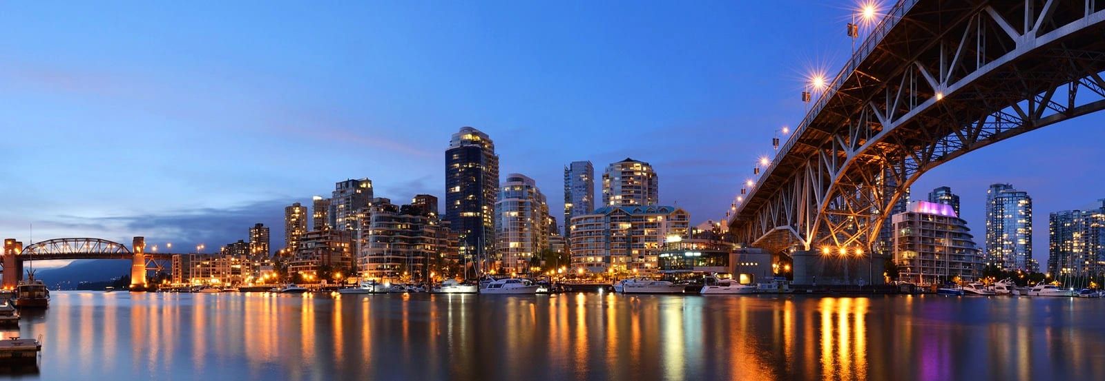 City view under Vancouver bridge with lights reflecting off river water during dusk