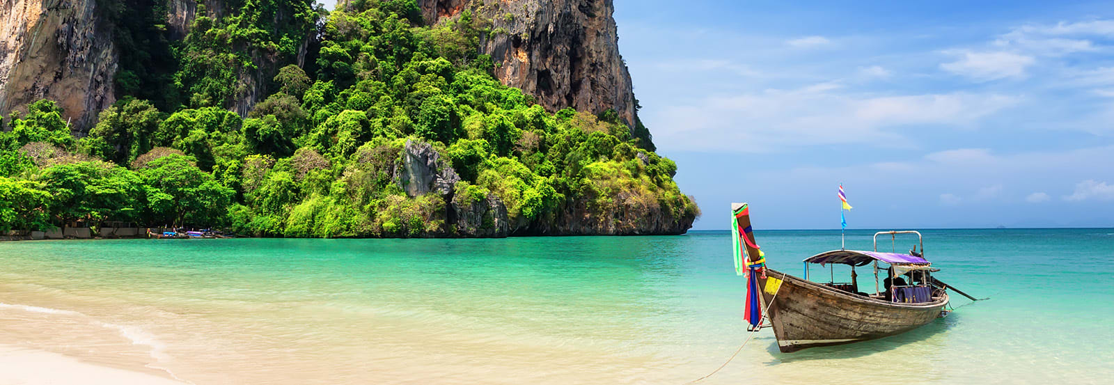 Wide angle shot of canoe half on shore half in water on an island beach located in Phuket