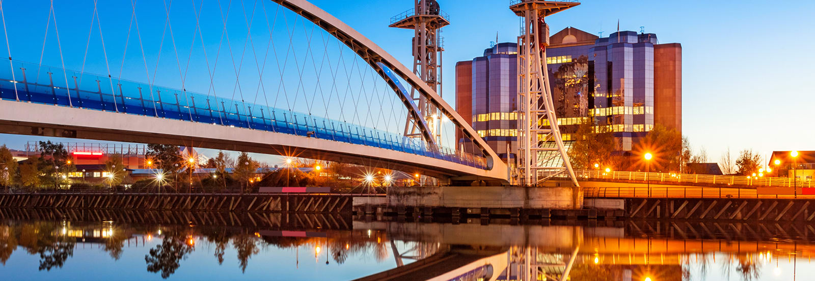 Milenium Bridge at dusk with streetlights turning on and reflecting the image in the water below