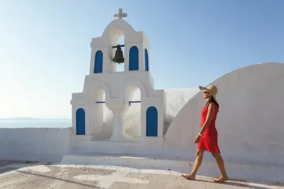 Woman in red dress walks through white Santorini buildings