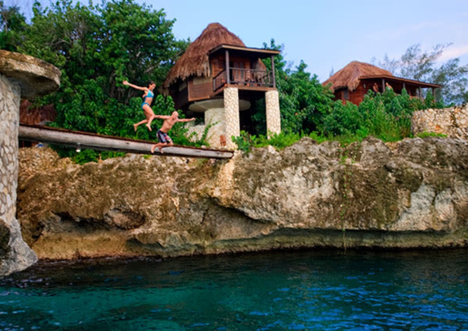 Two people in swimsuits diving off a high platform into the ocean
