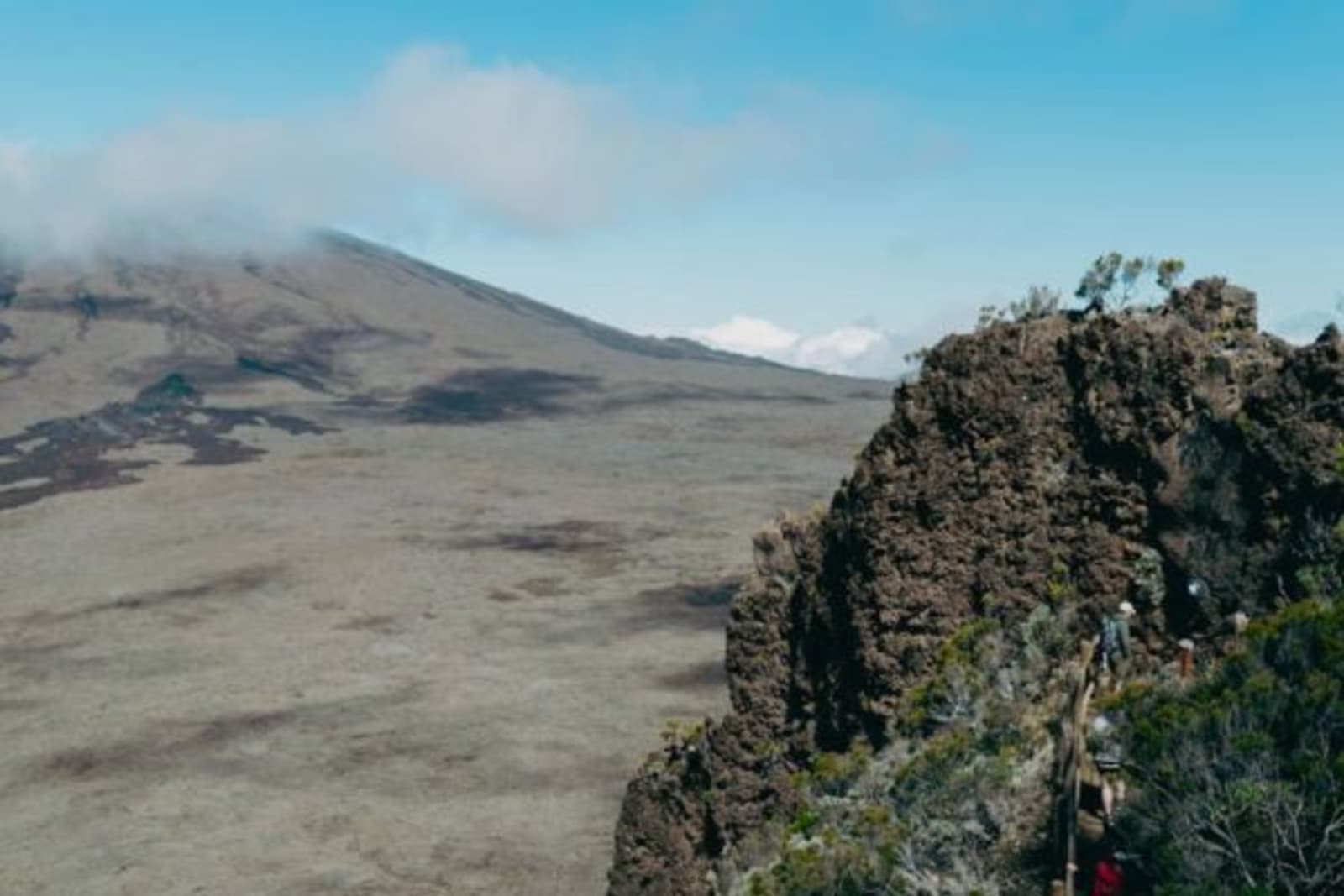 People hiking up a steep mountain with volcanic landscape in the background