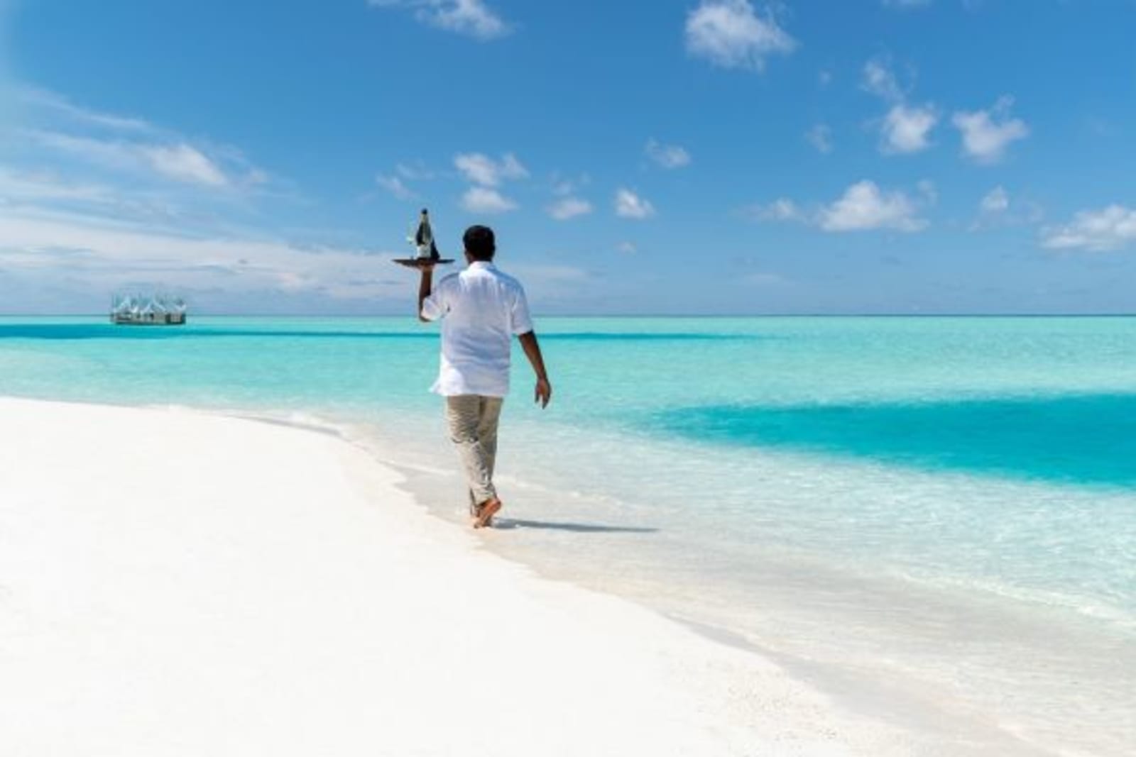 Male waiter carrying wine on dish in one hand walking along the beach