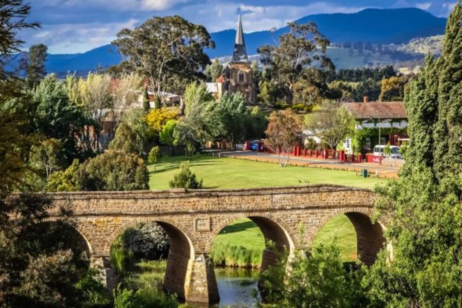 Arch bridge with greenery surrounding and a house in the background