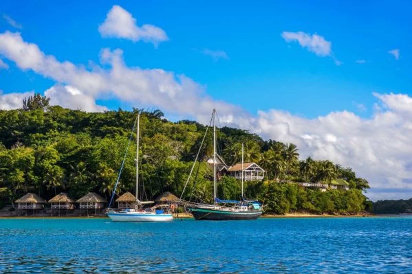 Boats sailing through ocean passing some huts in Vanuatu