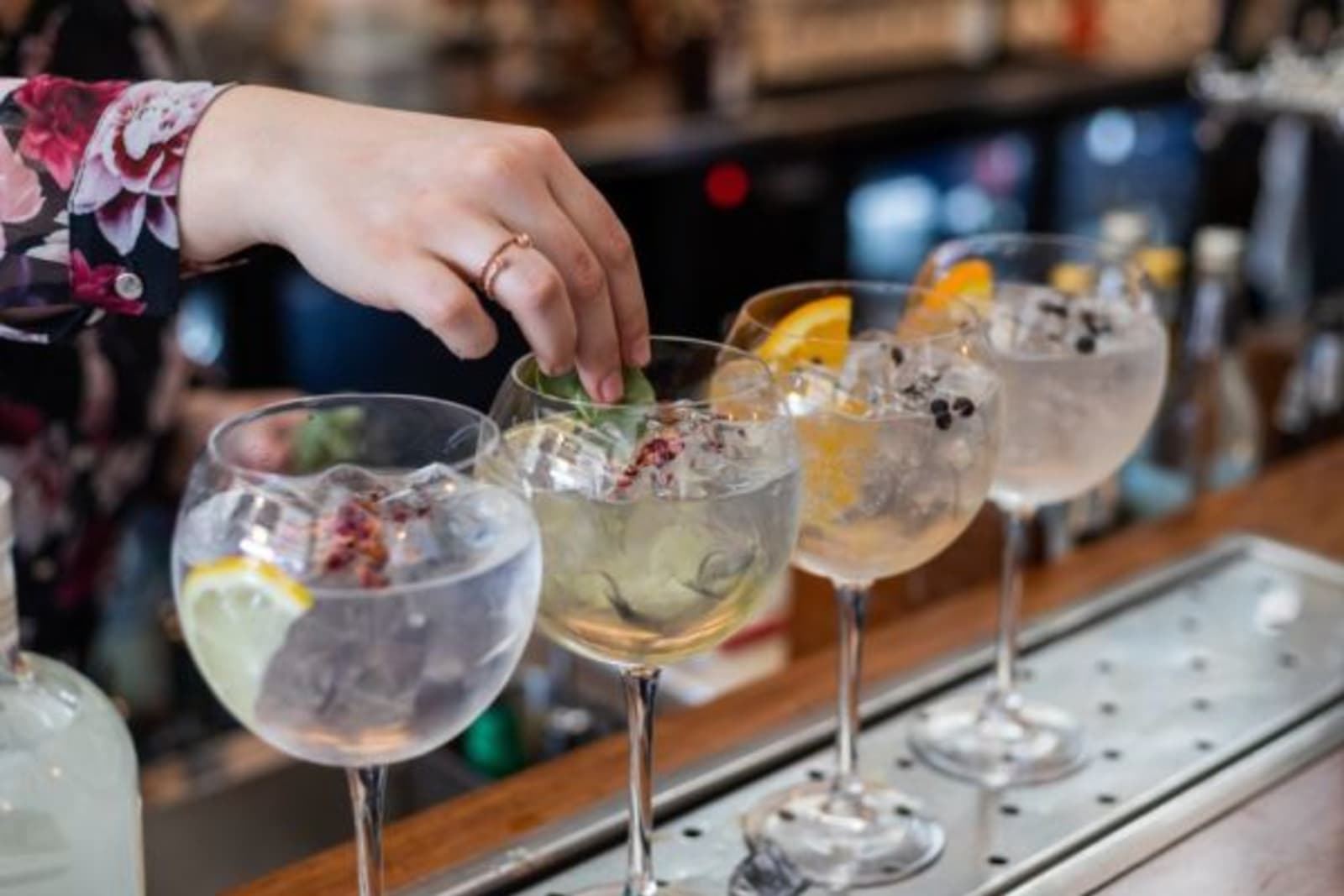4 cocktail drinks being made on a bar top, bar staff placing berries in glasses