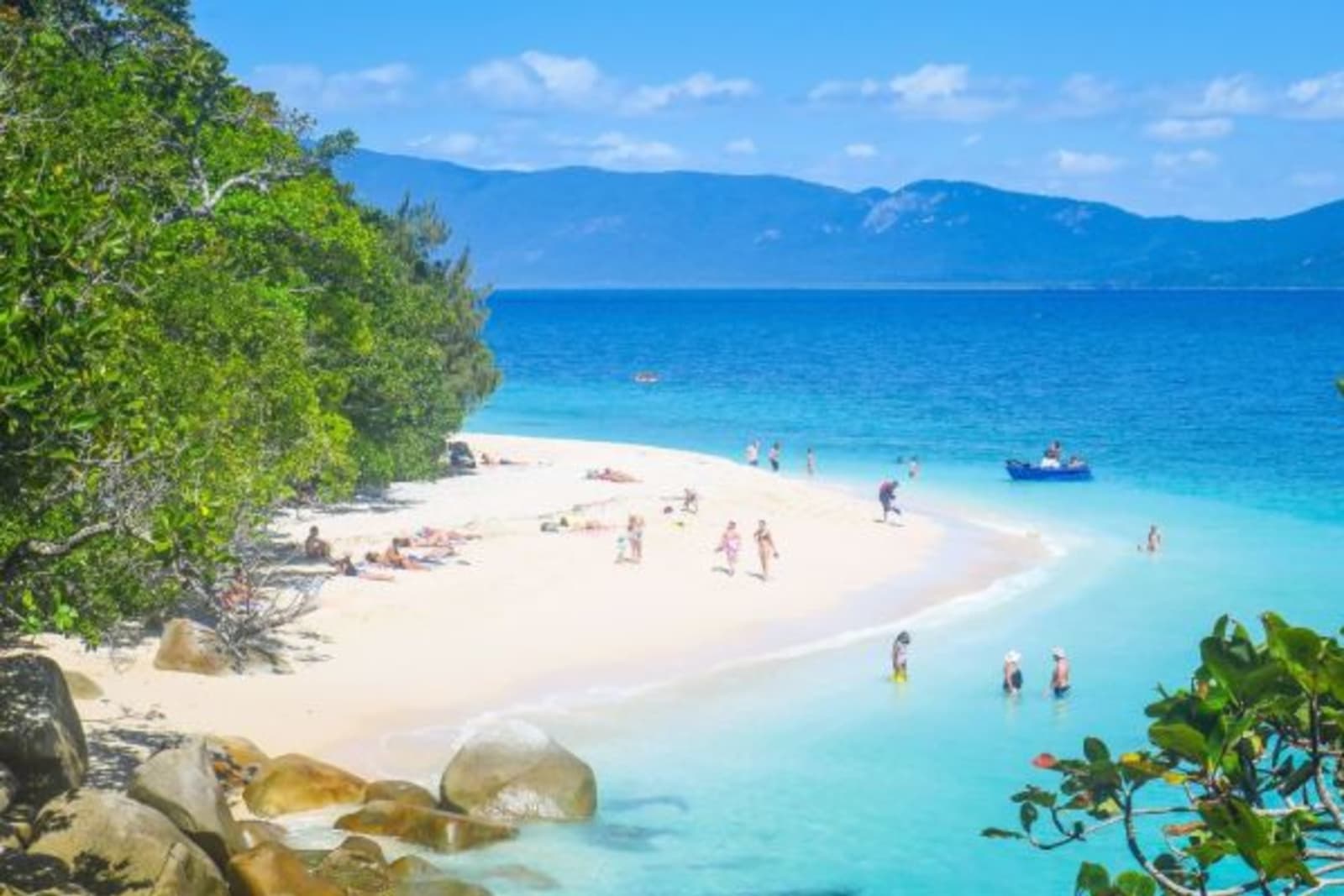 People swimming in crystal blue water with others walking along the sand