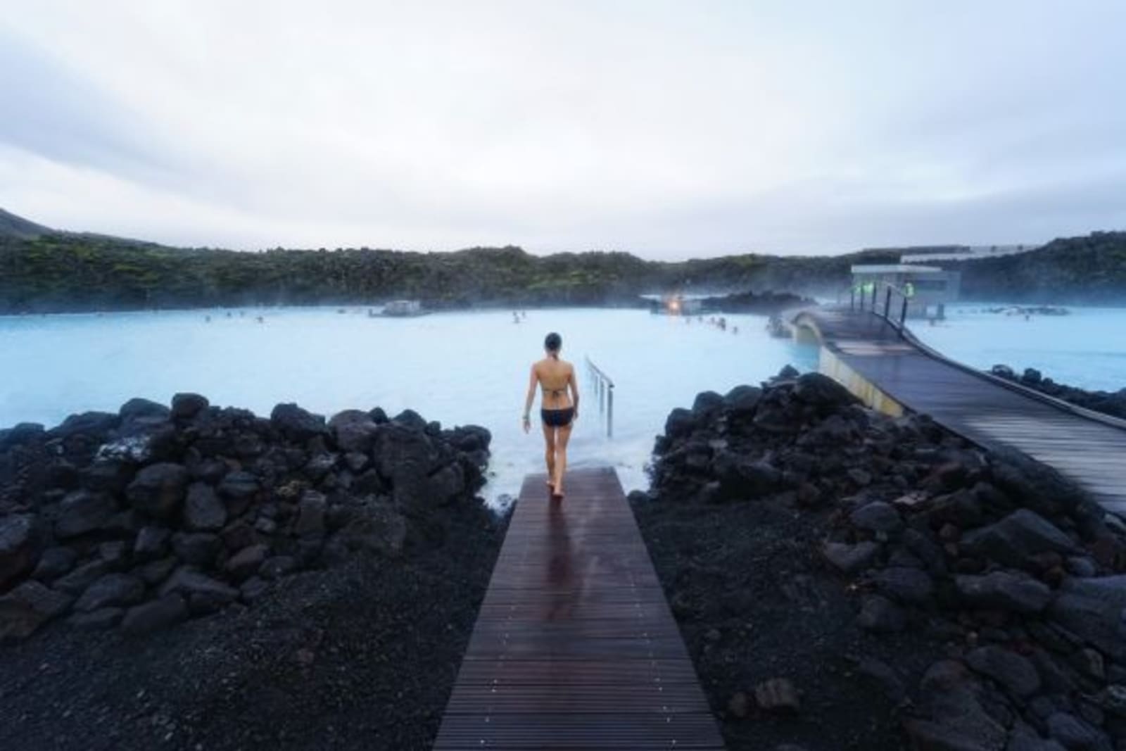 Woman walking towards Blue Lagoon on wooden pathway