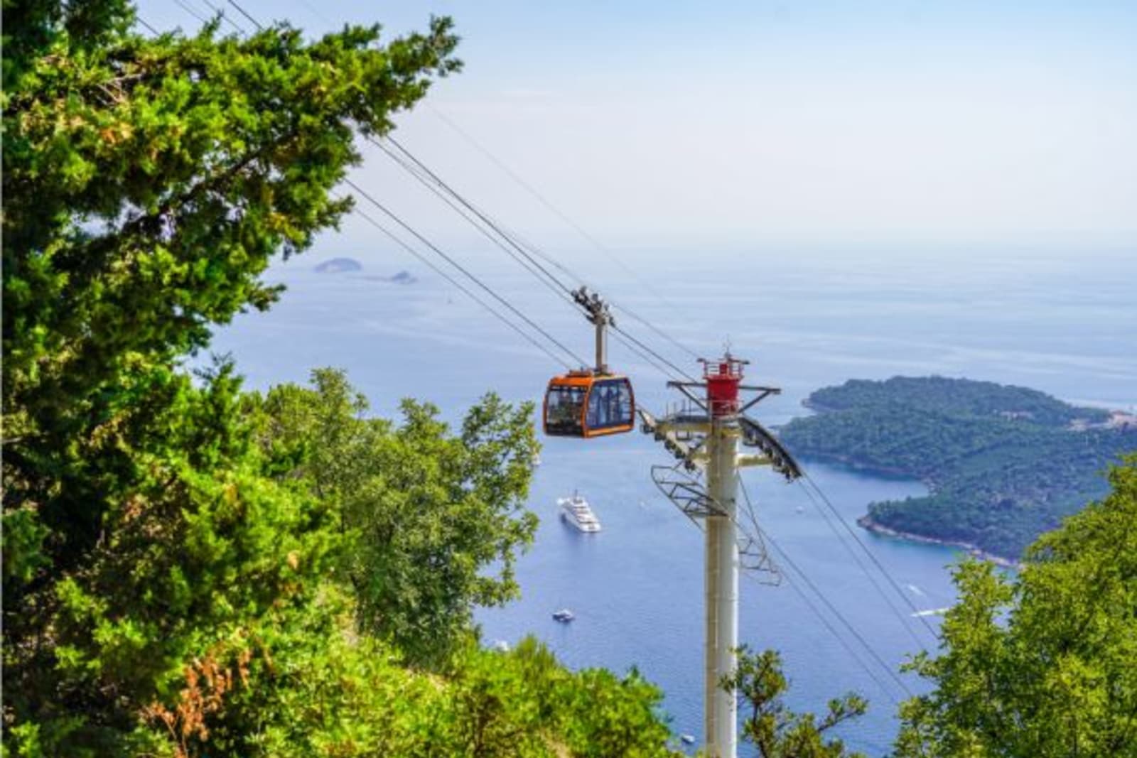 Distant shot of cable cart going up with ocean view in background