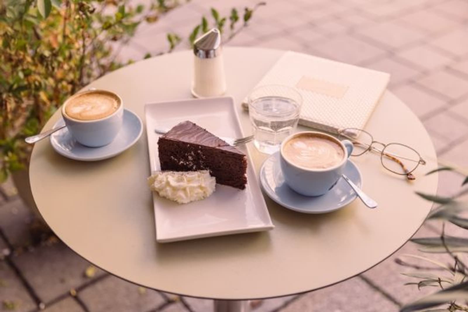 Small circular coffee table with two cups of coffee, glasses and cake on it