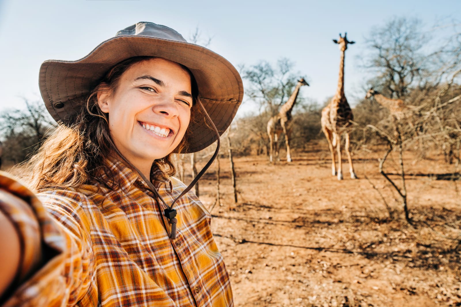 Happy female tourist enjoying the nature reserve and taking a selfie with giraffes in the background