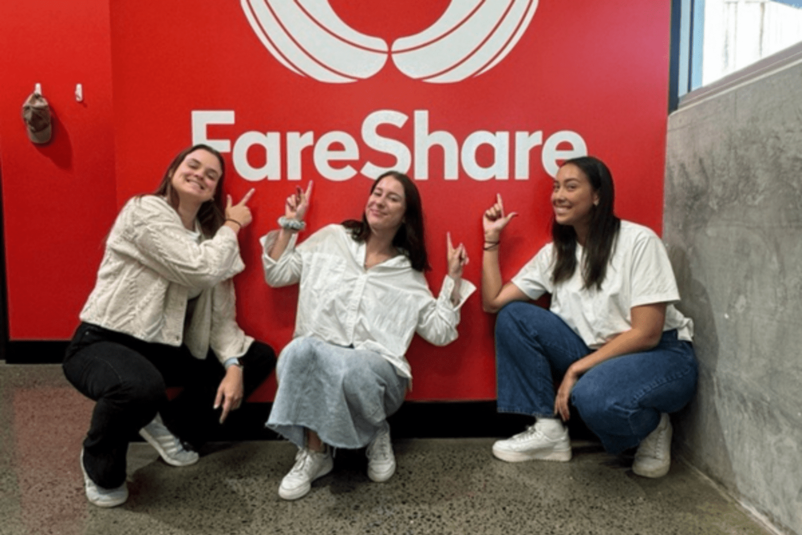 Three young women smiling, pointing to a Fair Share logo
