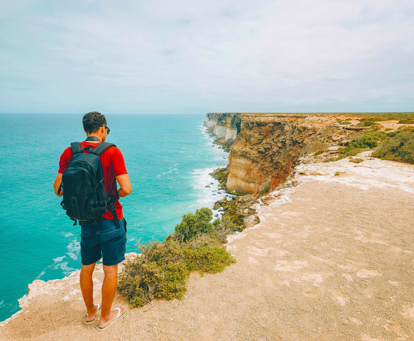 Man standing on the edge of a cliff looking down at the ocean