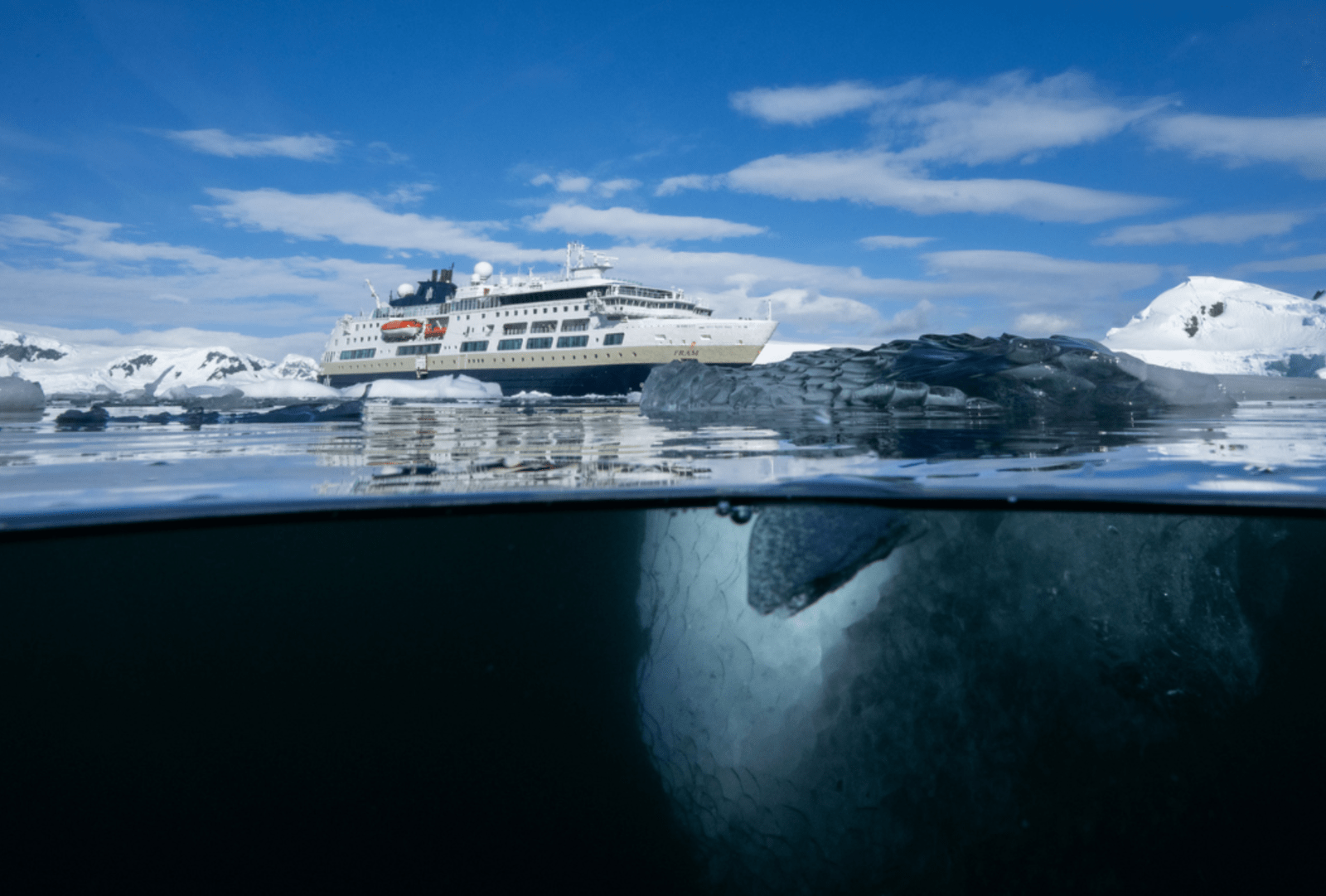 Expedition ship anchored among icebergs viewed half underwater showing ice floating beneath the surface