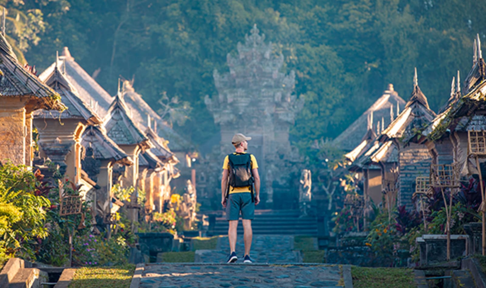 man walking away from camera down a path lined with small huts in bali