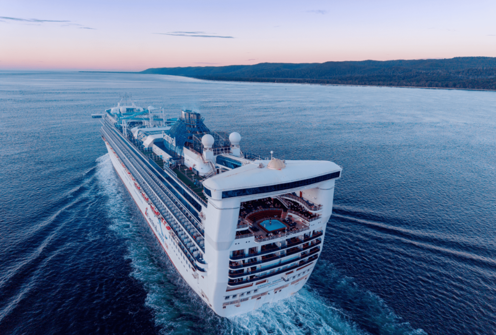 Carnival Encounter cruising along a calm coastline leaving a long white wake at dusk