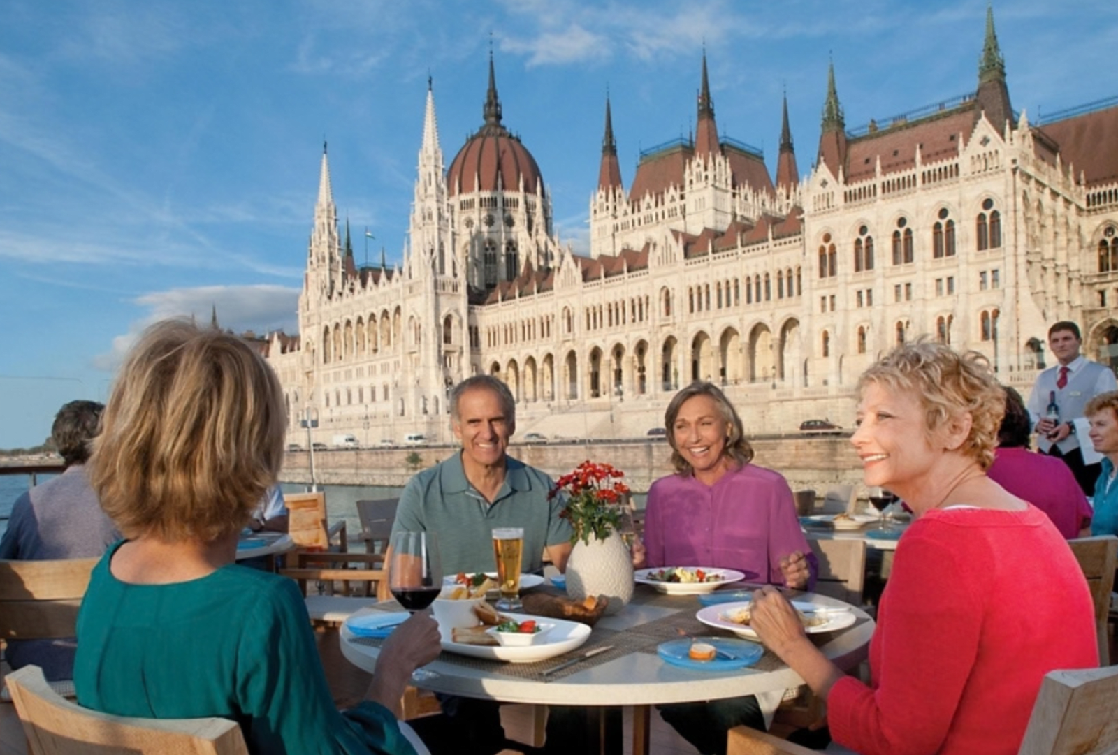 Friends dining on a river cruise deck overlooking the illuminated Hungarian Parliament Building in Budapest