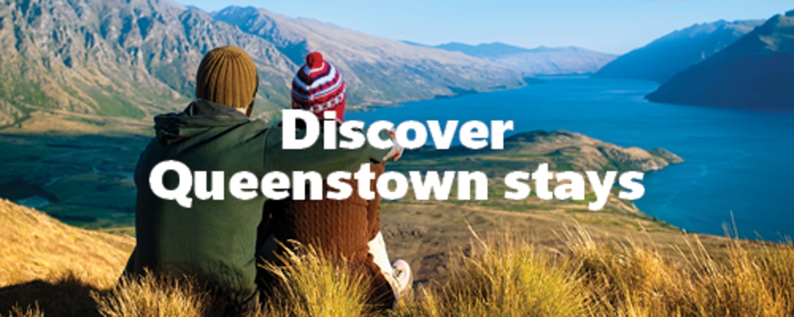 Discover Queenstown stays | couple sitting on a grassy hill looking out at a river