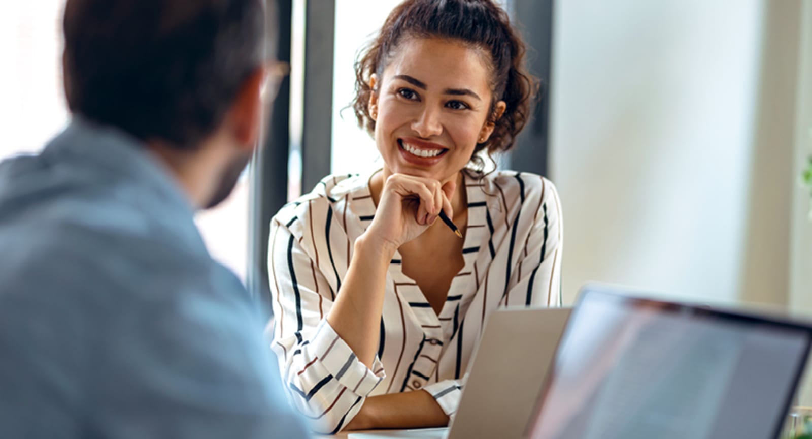Woman holding a pen smiling at a man with a laptop