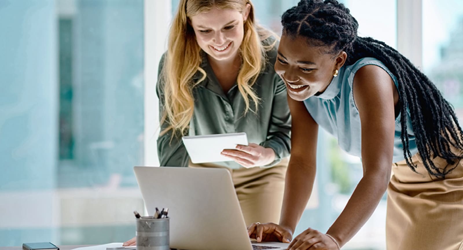 Two smiling businesswomen standing over a laptop