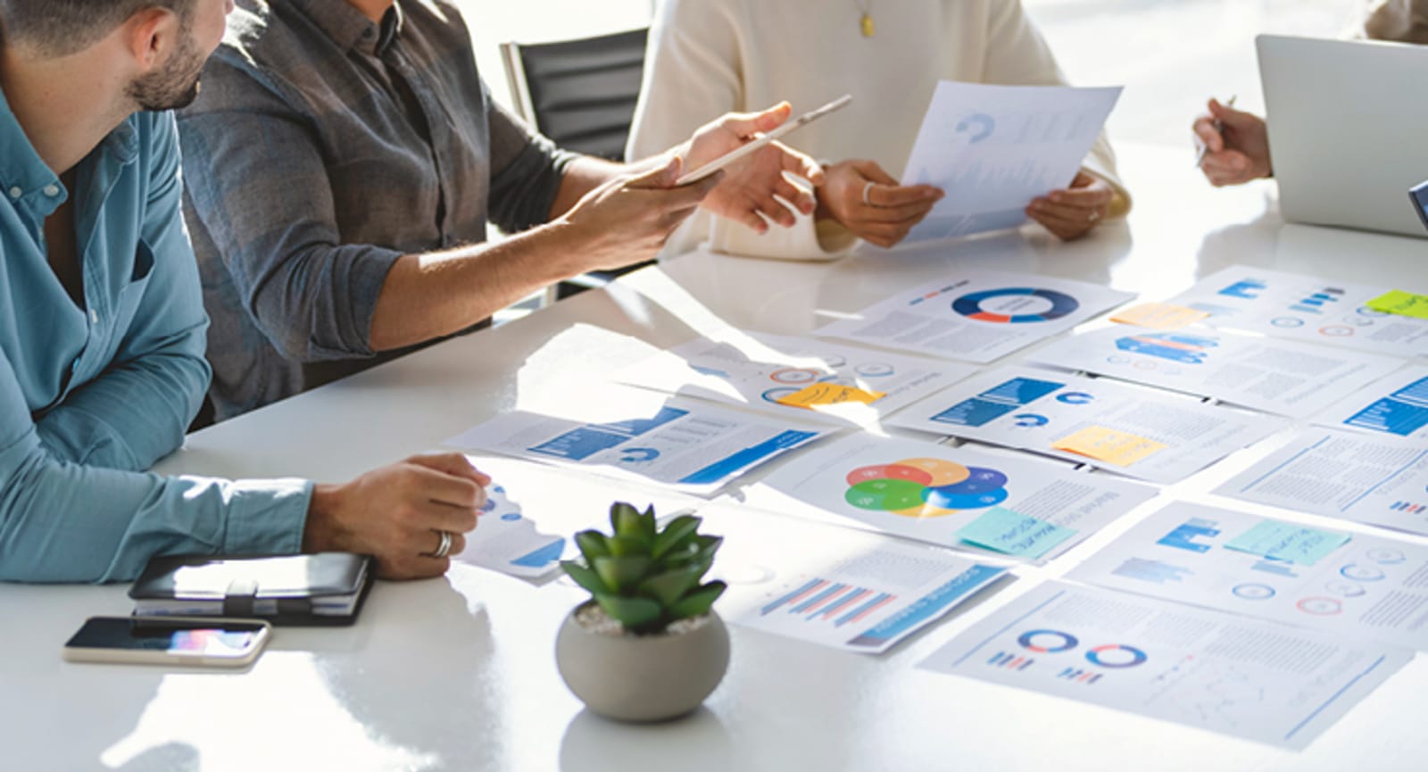 People sitting around a desk covered in printed graphs, reports and documents