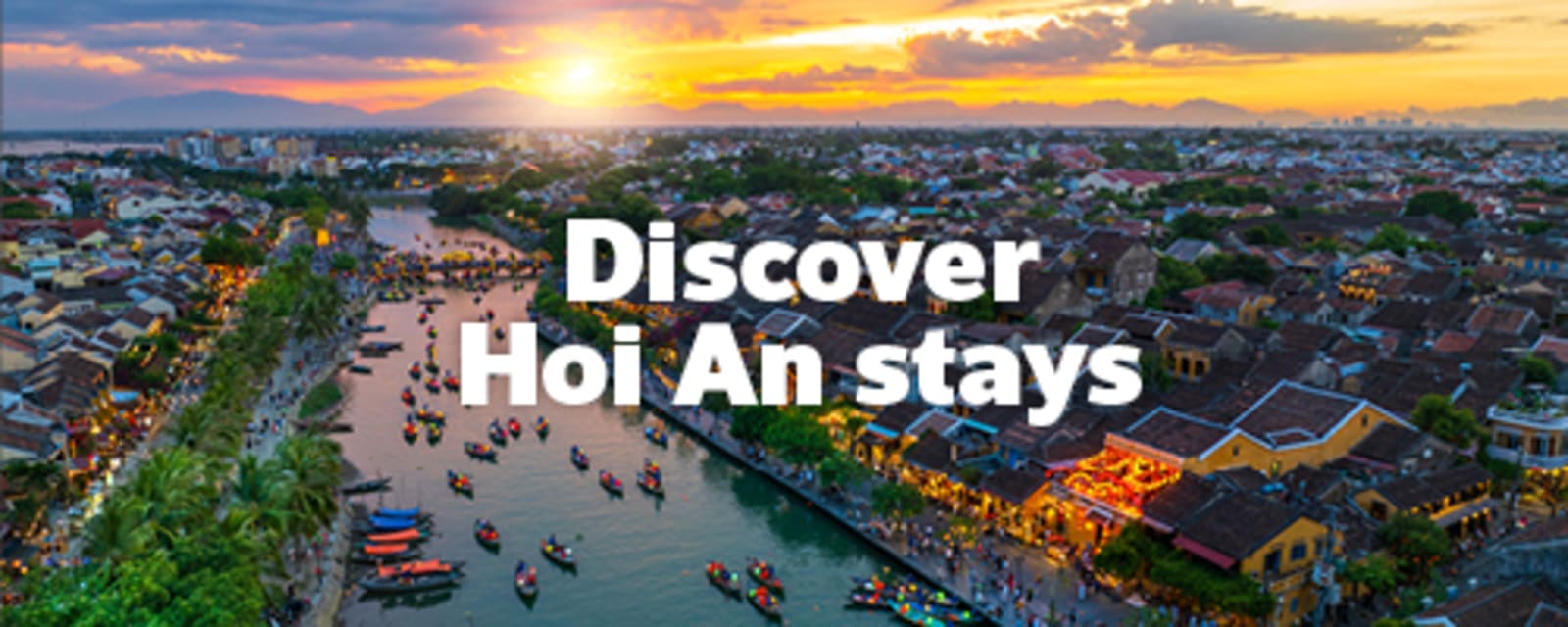 Hoai river in Hoi An at sunset, filled with rowboats and lined with tourists and busy market stalls