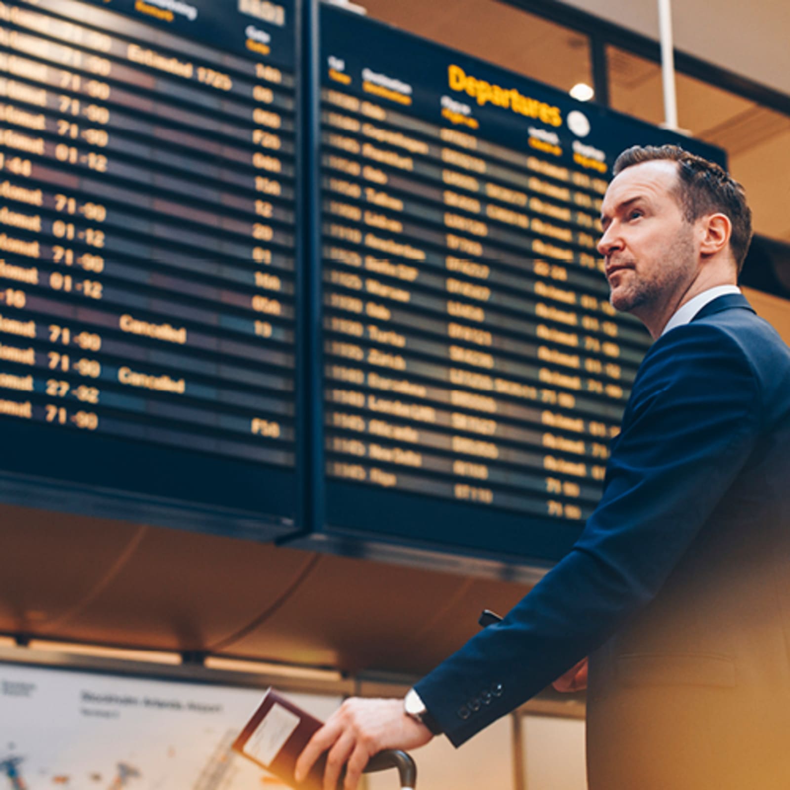 Man in suit waiting in front of a departures board in an airport
