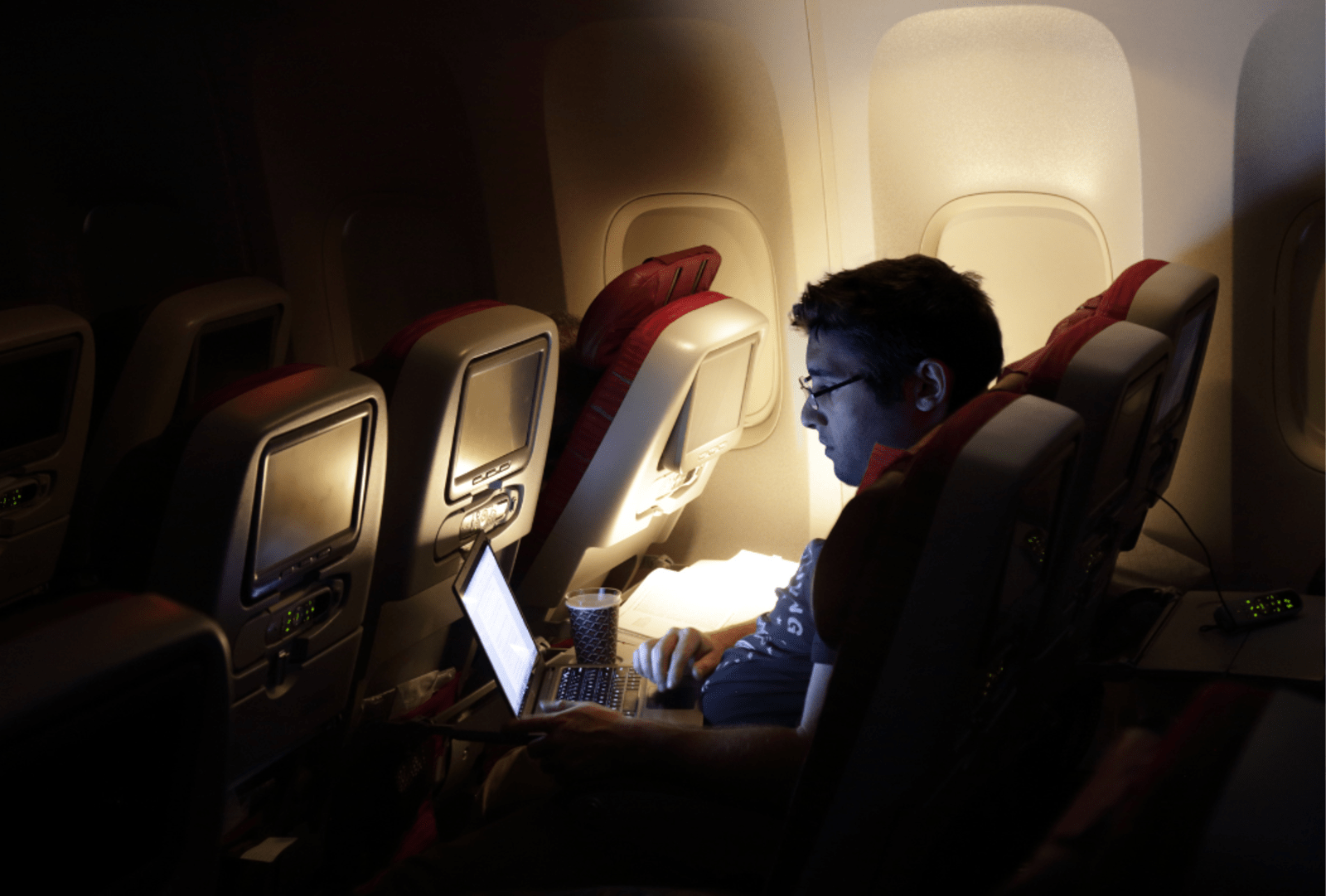 A man looking at laptop, on an aircraft.