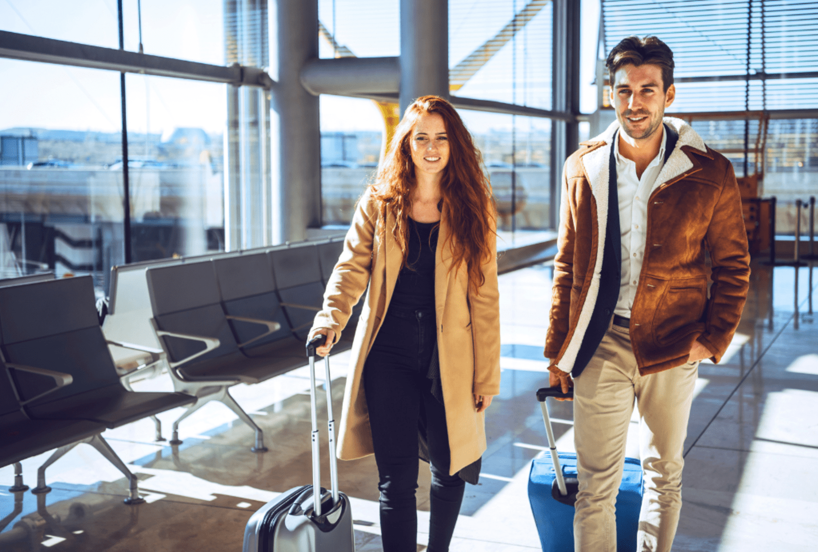 Smiling couple wheeling suitcases through a sunlit airport terminal ready for their business trip