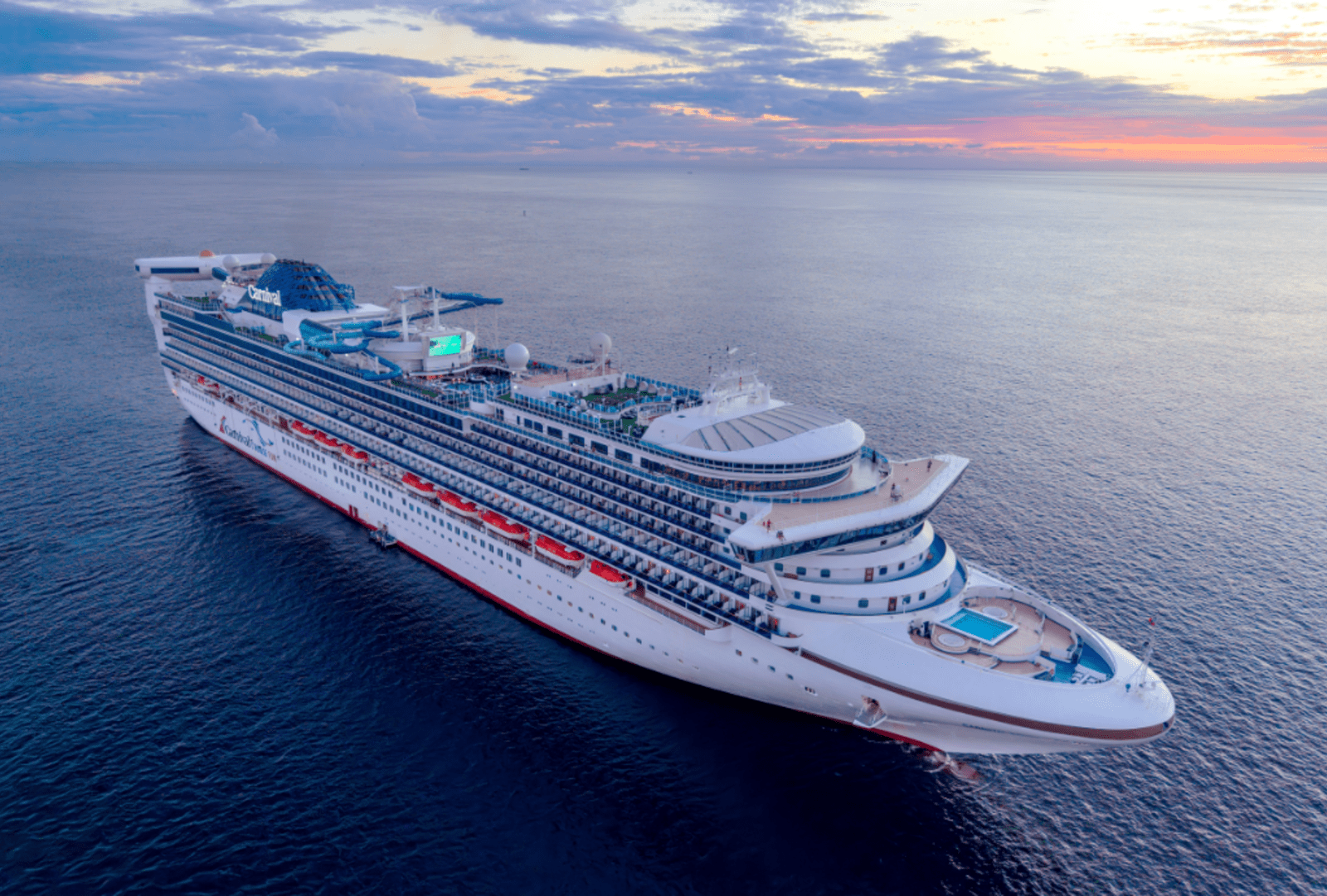 Carnival cruise ship sailing across calm ocean waters during a colourful sunset