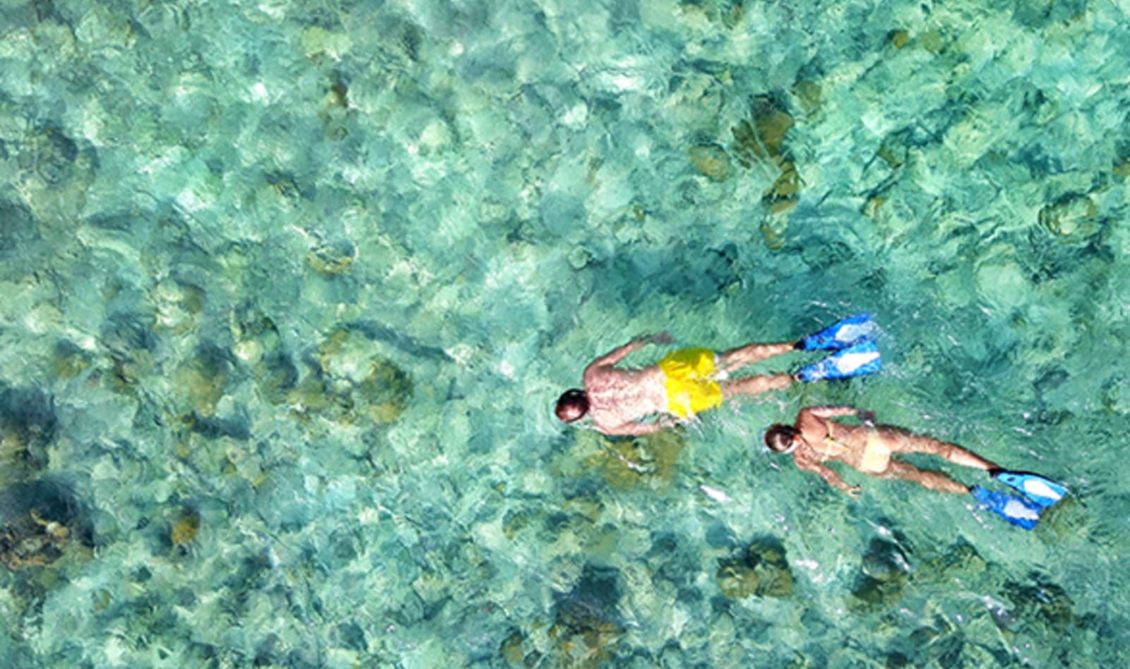 Top down view of two people snorkelling in crystal clear water
