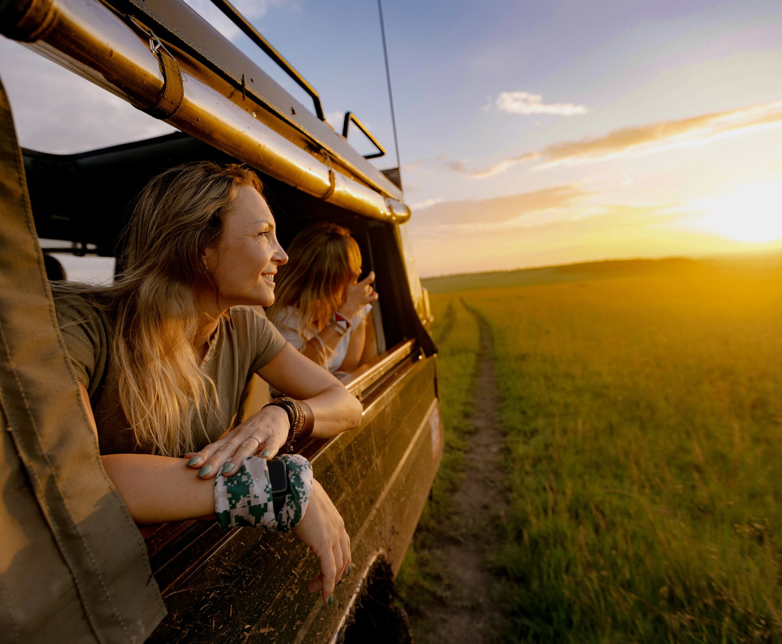 Women leaning out of a safari truck watching a sunset