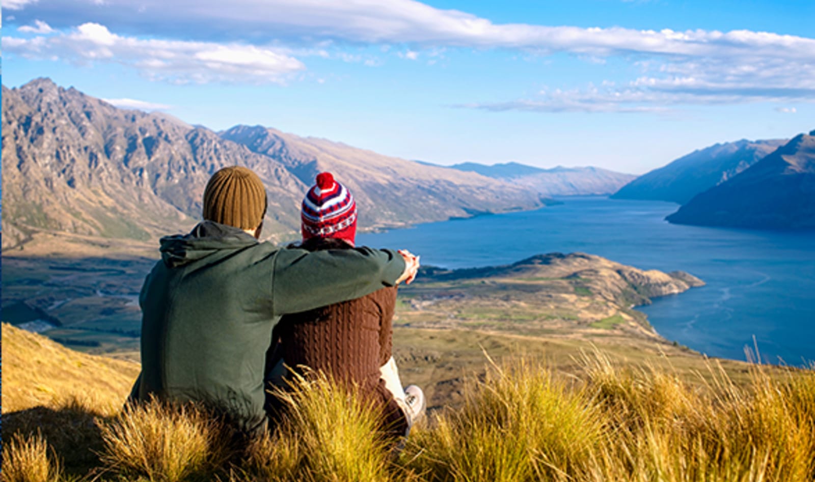 couple sitting on hill overlooking mountains and lake in queenstown
