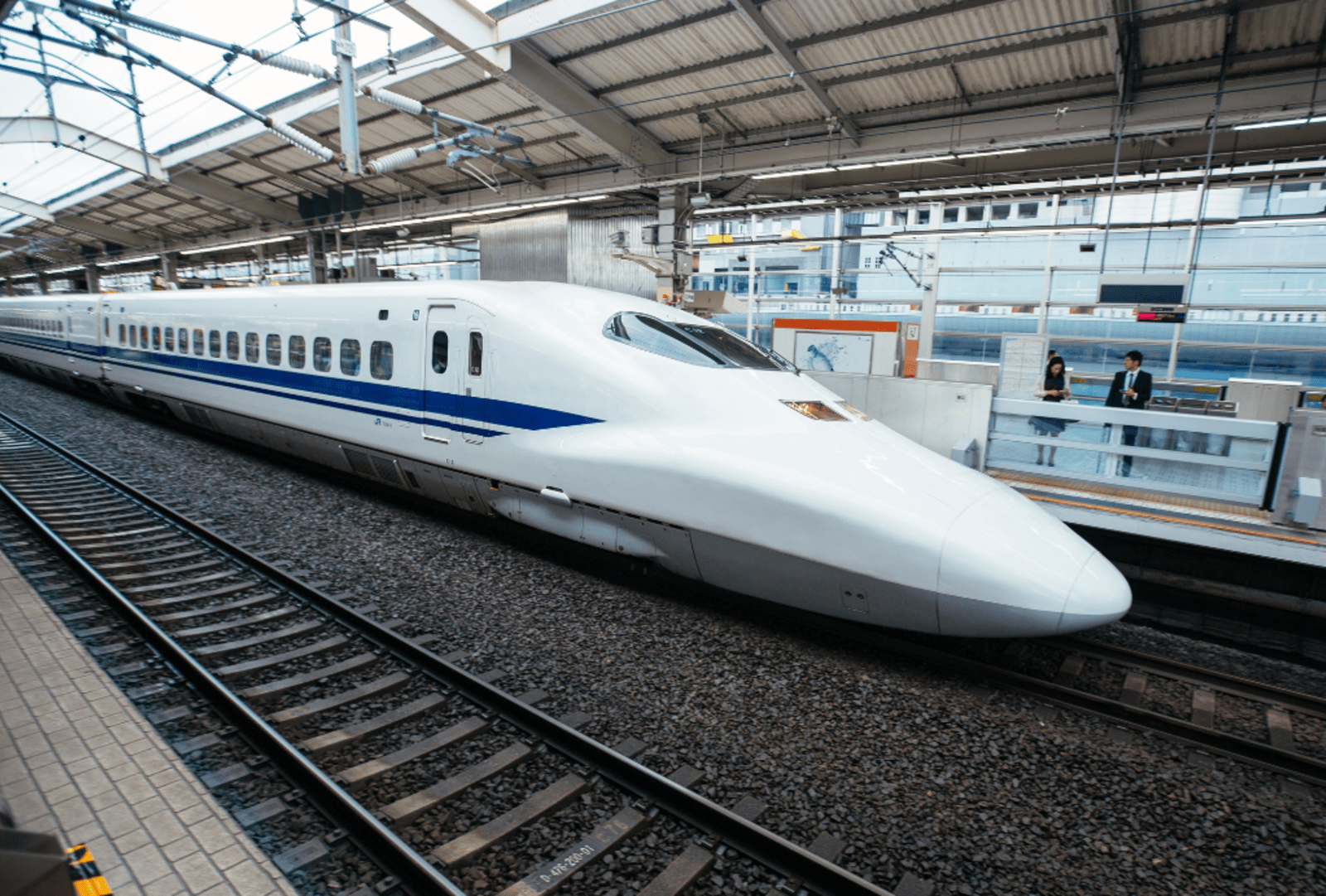 A white and blue Shinkansen bullet train stopped at a Japanese railway station platform